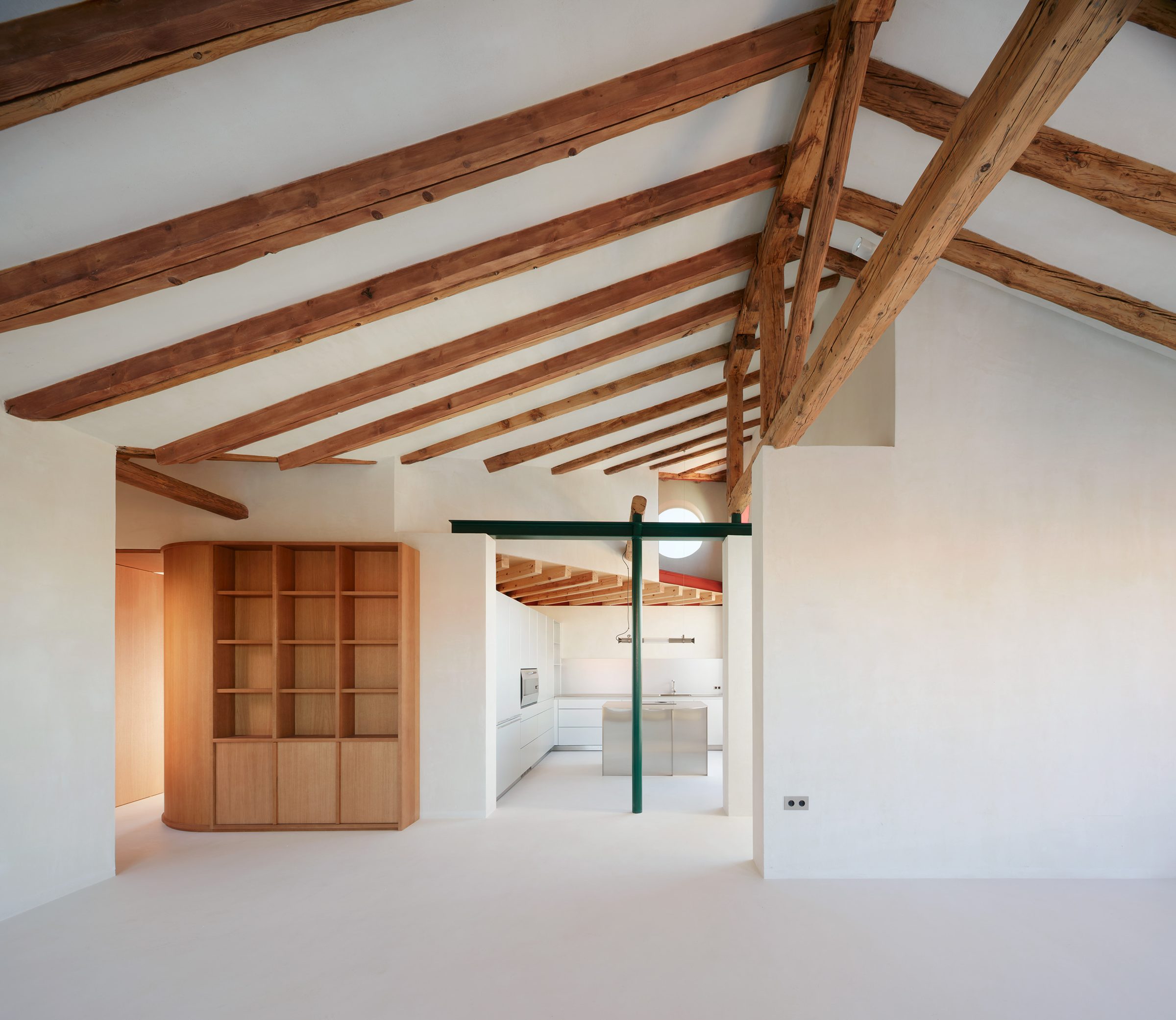 Ático rehabilitado con vigas de madera restauradas, microcemento y cocina blanca