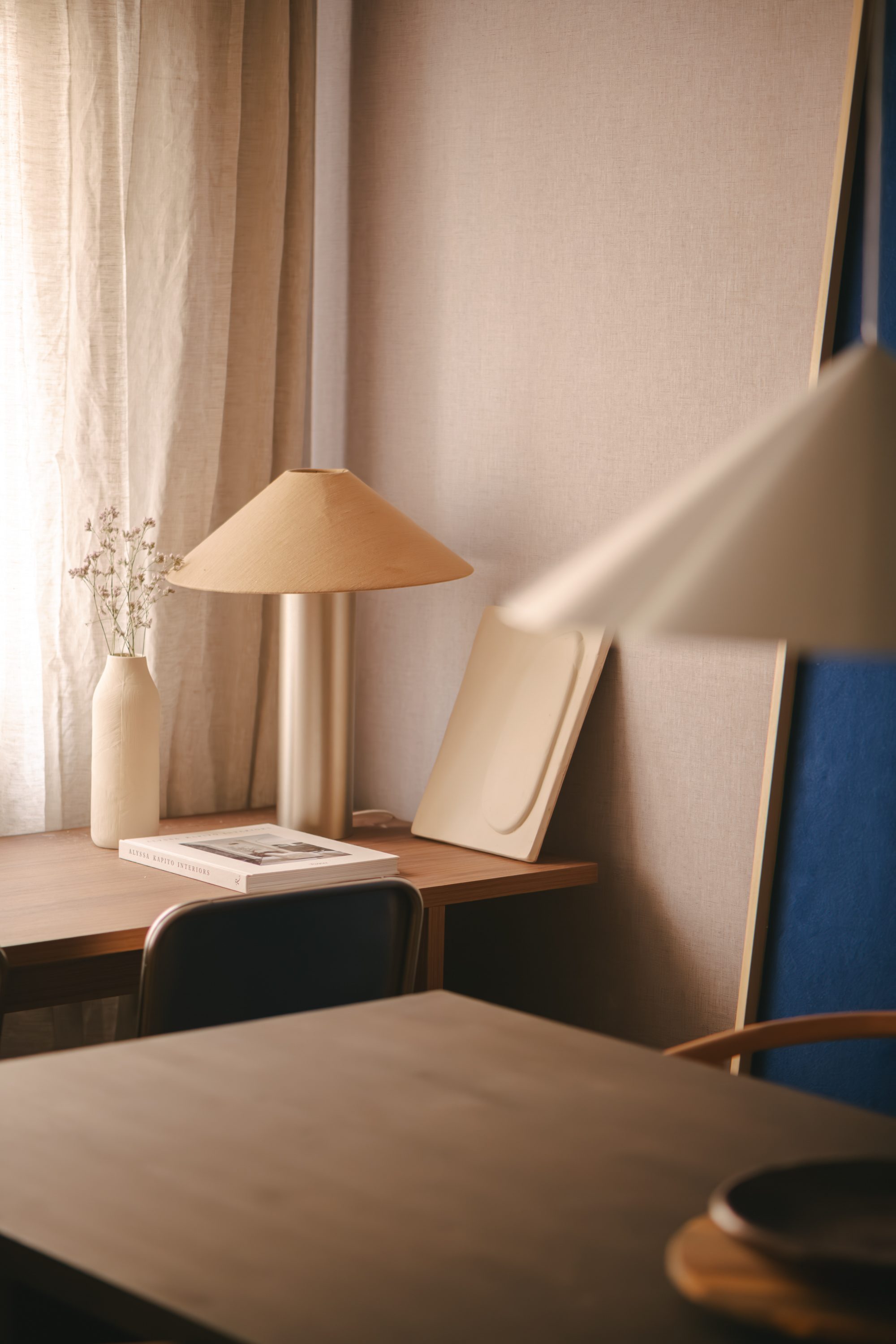 Rincón de escritorio con lámpara cónica, vajilla y libros de interiorismo